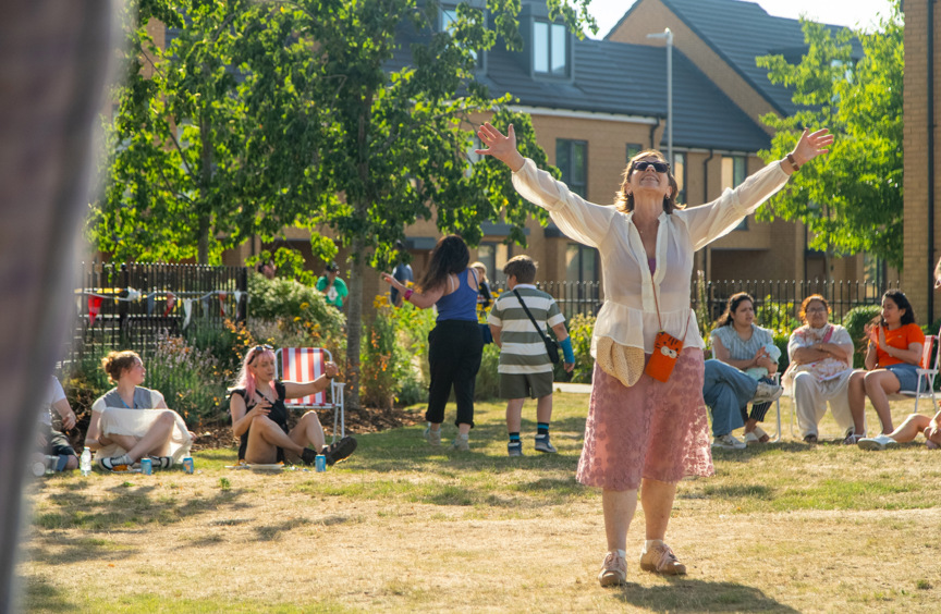 Woman with her arm above her head at an event in a park surrounded by a housing estate 