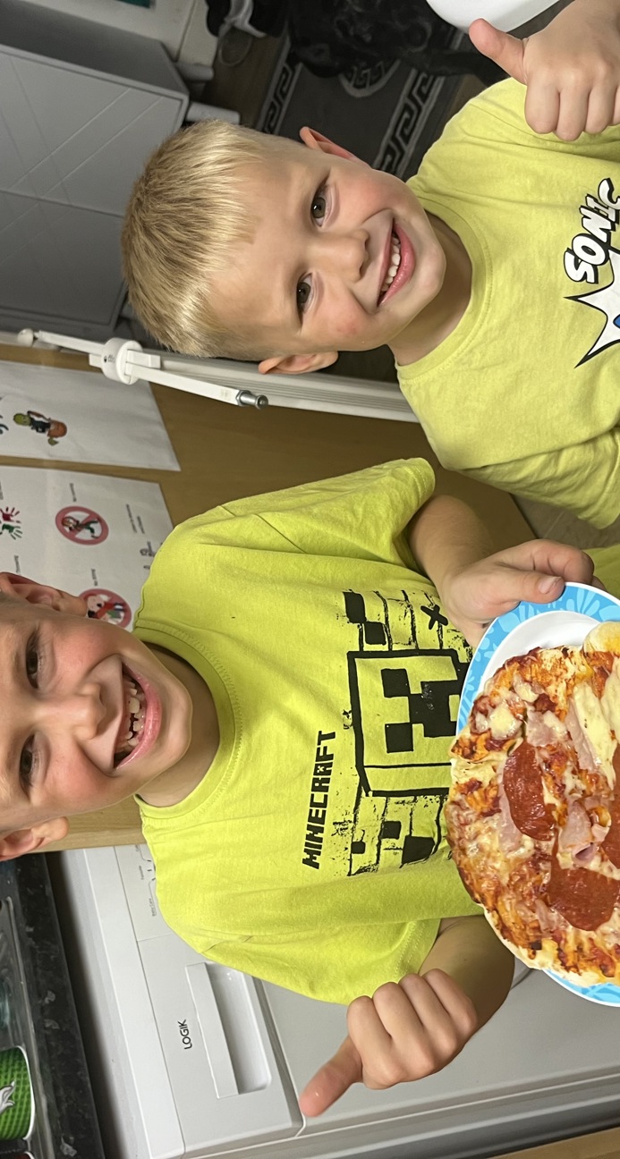 Two boys holding a pizza with their thumbs up