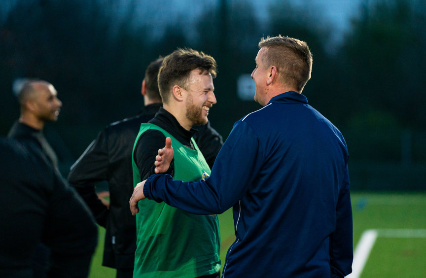 Two men about to hug on a football pitch