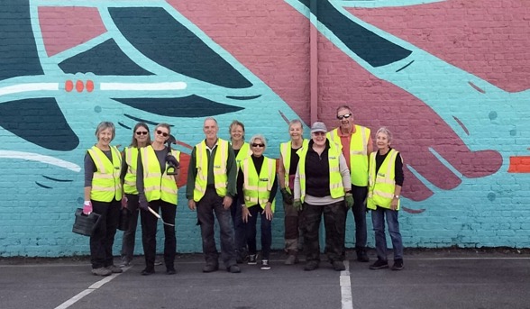 Gardening volunteers posing in high-vis infront of mural